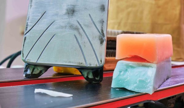 Ski wax iron and wax bars, colored orange and teal for different temperatures, laid on top of a pair of skis. 