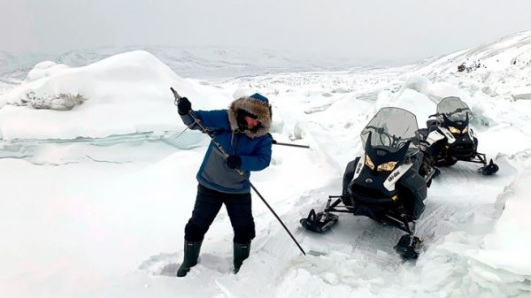 Man ice fishing beside snow mobile