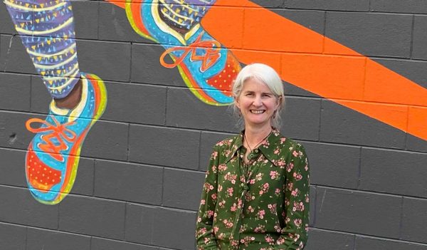 Kirsten Norquay standing in front of of a mural painted on a wall.