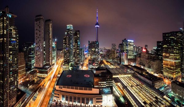 A panoramic high-angle view of central Toronto at night, with the illuminated CN Tower in the centre.
