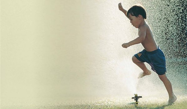 Child playing in large spray from a sprinkler.