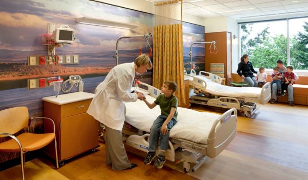 Doctor interacting with child patient in a patient room with small family in the background.