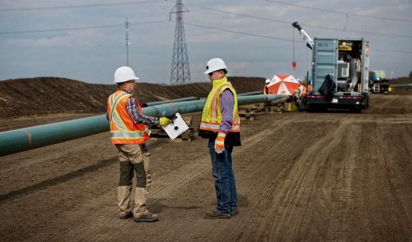 Two men talking near pipeline construction