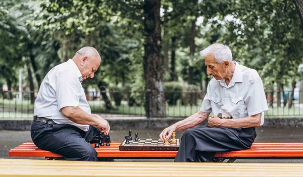 Two senior adult men playing chess on the bench outdoors in the park