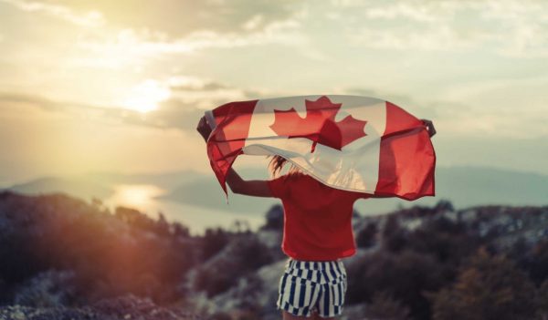 Person holding the Canada Flag over their shoulders, facing the sunset.