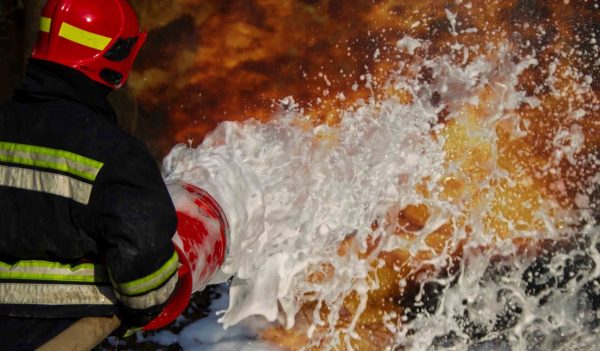 Firefighter spraying a suppressant foam on a fire.