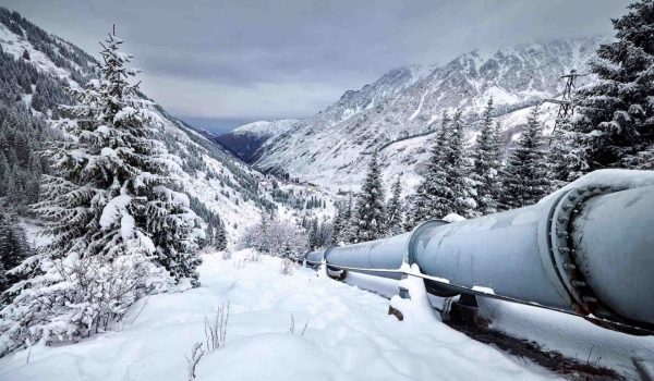 Pipeline running through a remote area in the mountains with snow on the ground.