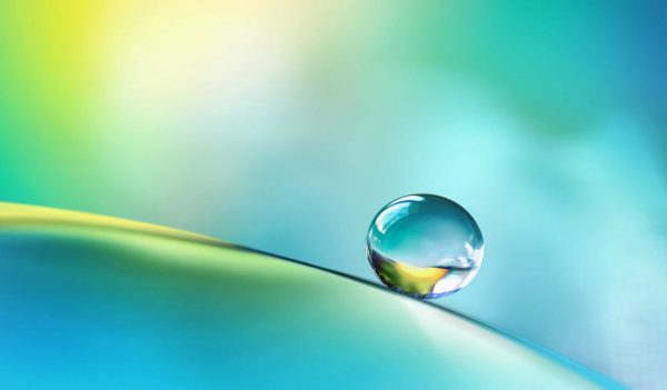 Transparent bright drop of water on smooth surface in blue and yellow colors.