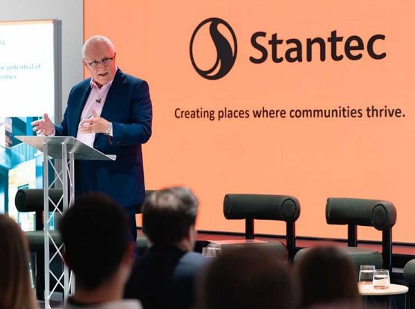 Sir Michael Lyons standing at a podium deliverig a speach with Stantec branded graphics in the background.