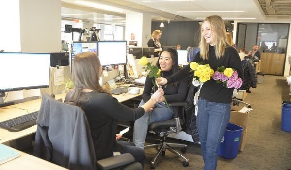 A woman giving flowers to 2 of her co-workers