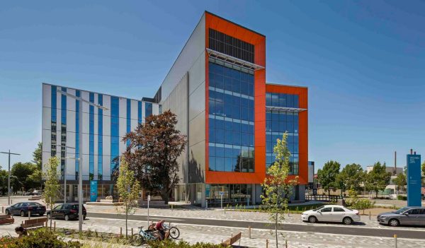 Exterior view of building from the front with red architectural higlights against a blue sky.