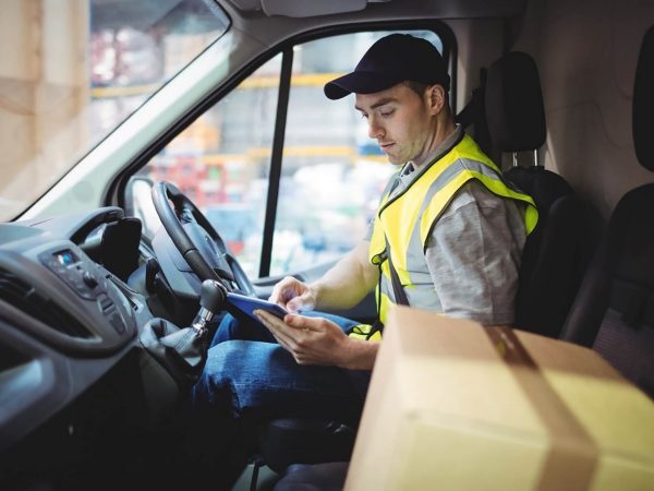 Male delivery driver wearing a hi-vis vest looking at a smart tablet inside the van