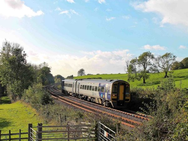 Blue skies, green countryside with a railway line running through the field with a train passing through