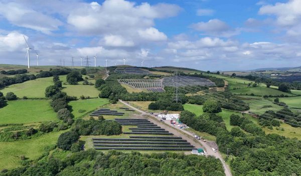 Image of solar farm from bird eye view, showing green fields and a cloudy blue sky.