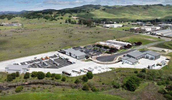 Aerial view of the buildings, parking, and surrounding site with hills and plantings