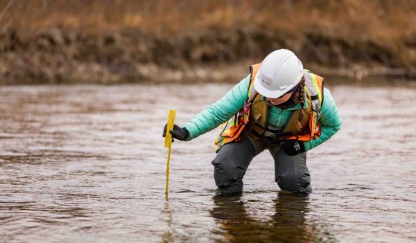 Environmental Scientist, wearing a safety vest and hard hat, taking measurements in the river