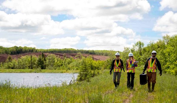 Alicia Fancey, Kelly Fraser and Shaun Helpard walking near a pond wearing PPE, conducting environmental testing.