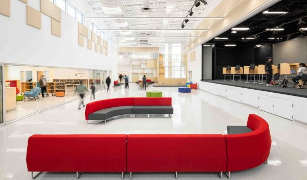 Large entrance multi-purpose hall with library on one side, a stage on the other, and soft seating in the middle