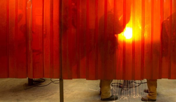 Welders working behind a protective curtain.