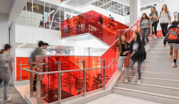 Interior of students walking on a staircase with clear, red panels.