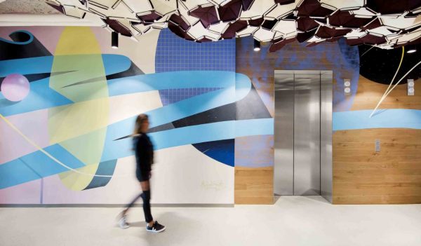 Person walking by a bank of elevators with a graphic mural on the wall.