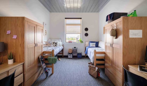 Interior student dorm room for two with beds, a wardrobe and desk on each side of the room.