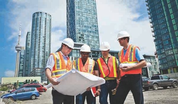 People view drawings on a construction site with buildings in the background