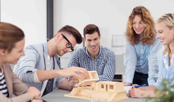 Architecture students interacting with a building model on a table.